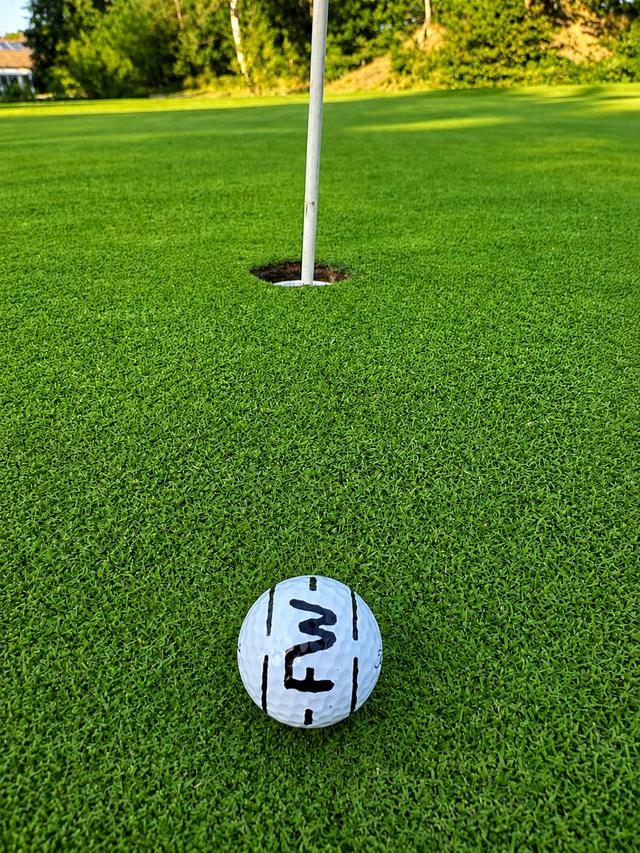 Golfball mit Initialen FW auf dem Grün nahe der Fahne
